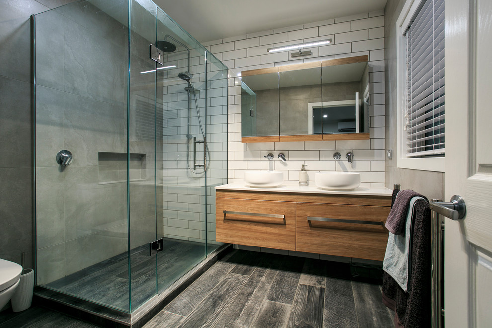 Inspiration for a mid-sized contemporary master bathroom with medium wood cabinets, a corner shower, ceramic tile, ceramic floors, a vessel sink, engineered quartz benchtops, grey floor, a hinged shower door, white benchtops, flat-panel cabinets, white tile and a double vanity.