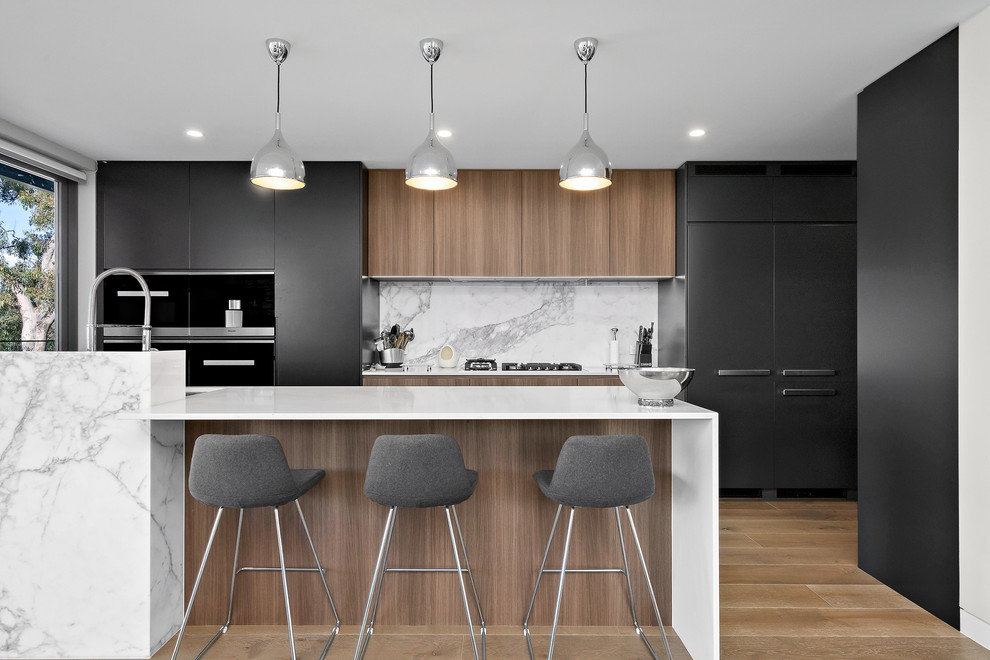 Inspiration for a large contemporary galley open plan kitchen in Sydney with an integrated sink, black cabinets, quartz benchtops, grey splashback, marble splashback, stainless steel appliances, medium hardwood floors, with island, brown floor, white benchtop and flat-panel cabinets.
