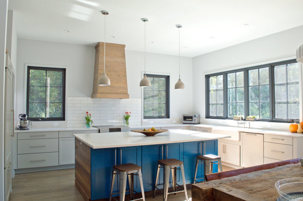 Open concept kitchen - rustic u-shaped light wood floor and brown floor open concept kitchen idea with a farmhouse sink, flat-panel cabinets, gray cabinets, quartzite countertops, white backsplash, subway tile backsplash, paneled appliances, an island and white countertops