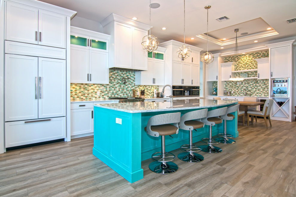 Expansive beach style l-shaped kitchen in Miami with a farmhouse sink, shaker cabinets, white cabinets, green splashback, porcelain splashback, with island, brown floor and grey benchtop.