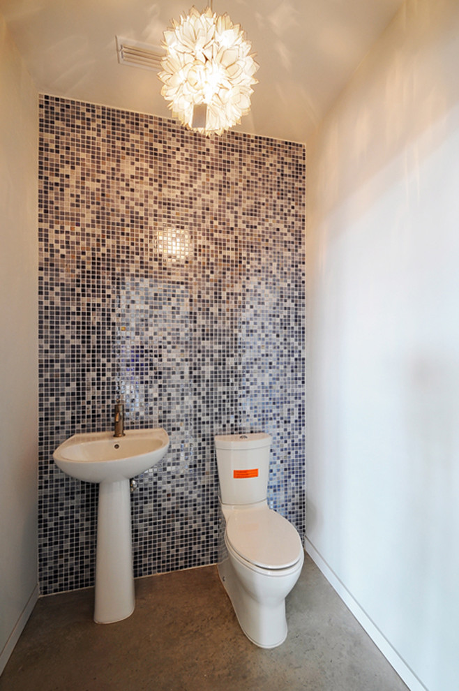 This is an example of a small contemporary powder room in Austin with a pedestal sink, a two-piece toilet, multi-coloured tile, concrete floors and mosaic tile.