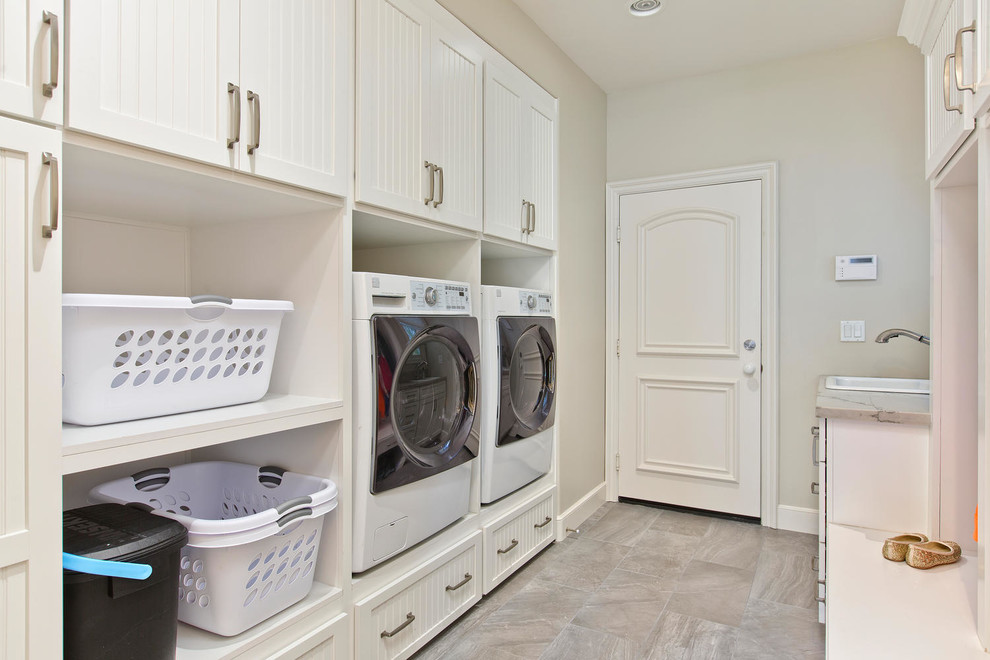 Design ideas for a large beach style u-shaped laundry room in Denver with a farmhouse sink, recessed-panel cabinets, white cabinets, quartzite benchtops, grey splashback, stone tile splashback, medium hardwood floors and brown floor.