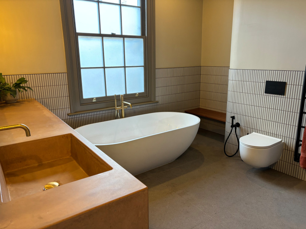Inredning av ett modernt stort orange oranget badrum för barn, med öppna hyllor, orange skåp, ett fristående badkar, en öppen dusch, en vägghängd toalettstol, orange kakel, keramikplattor, vita väggar, klinkergolv i porslin, ett konsol handfat, bänkskiva i betong, grått golv och med dusch som är öppen