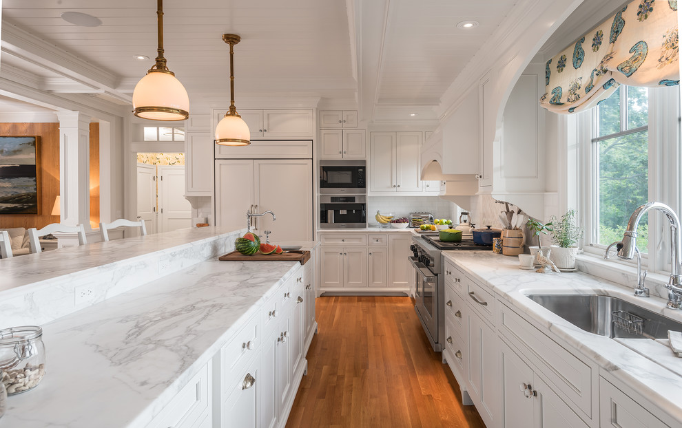 Inspiration for a large beach style kitchen in Portland Maine with an undermount sink, white cabinets, marble benchtops, recessed-panel cabinets, white splashback, subway tile splashback, panelled appliances, medium hardwood floors and orange floor.