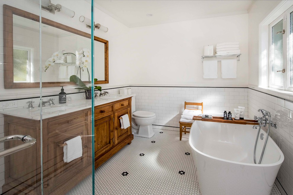 Design ideas for a country master bathroom in San Francisco with recessed-panel cabinets, medium wood cabinets, a freestanding tub, a two-piece toilet, subway tile, white walls, an undermount sink, white floor, white benchtops and white tile.