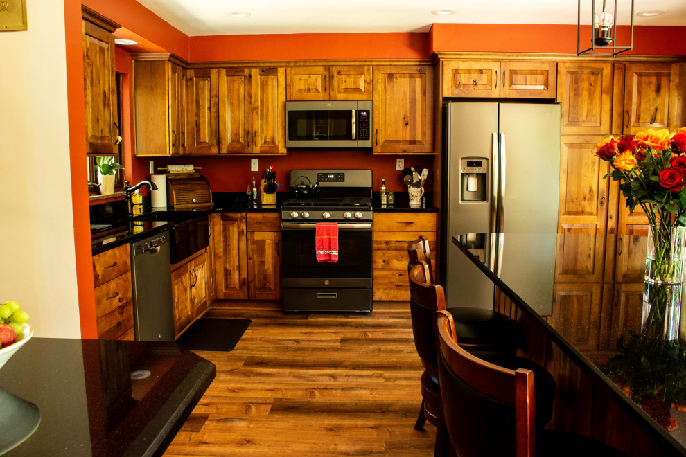 Example of a large mountain style u-shaped medium tone wood floor and brown floor open concept kitchen design with a farmhouse sink, raised-panel cabinets, medium tone wood cabinets, quartz countertops, stainless steel appliances, an island and black countertops