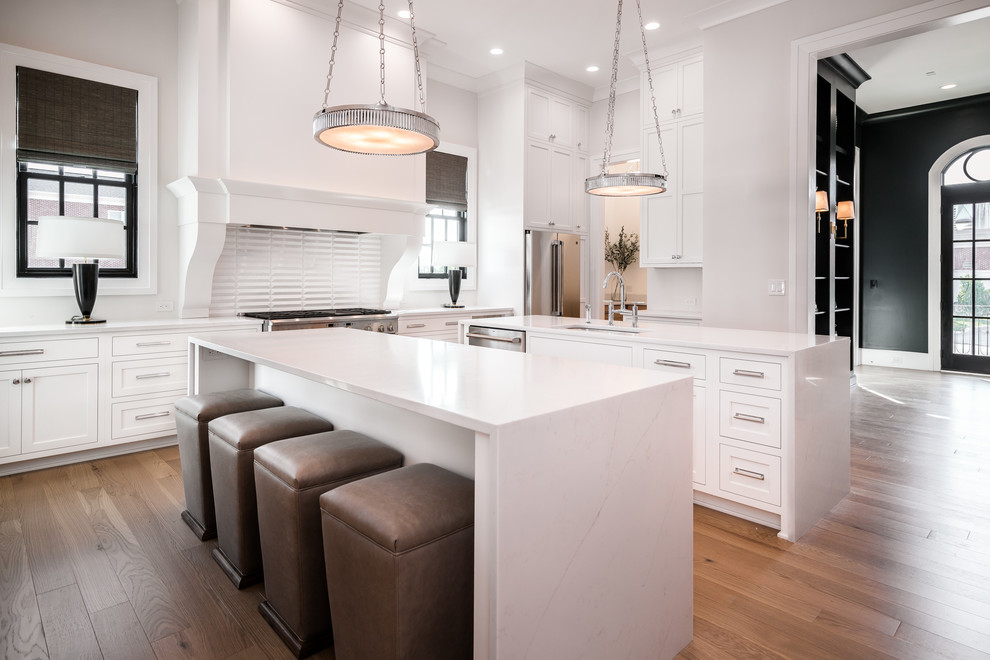Design ideas for a transitional kitchen in Louisville with an undermount sink, shaker cabinets, white cabinets, white splashback, stainless steel appliances, light hardwood floors, multiple islands, beige floor and white benchtop.
