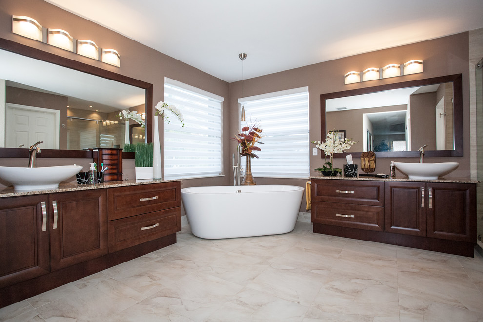 Traditional bathroom in Miami with a vessel sink, raised-panel cabinets, medium wood cabinets, granite benchtops, a freestanding tub, a curbless shower, a one-piece toilet, multi-coloured tile and porcelain tile.