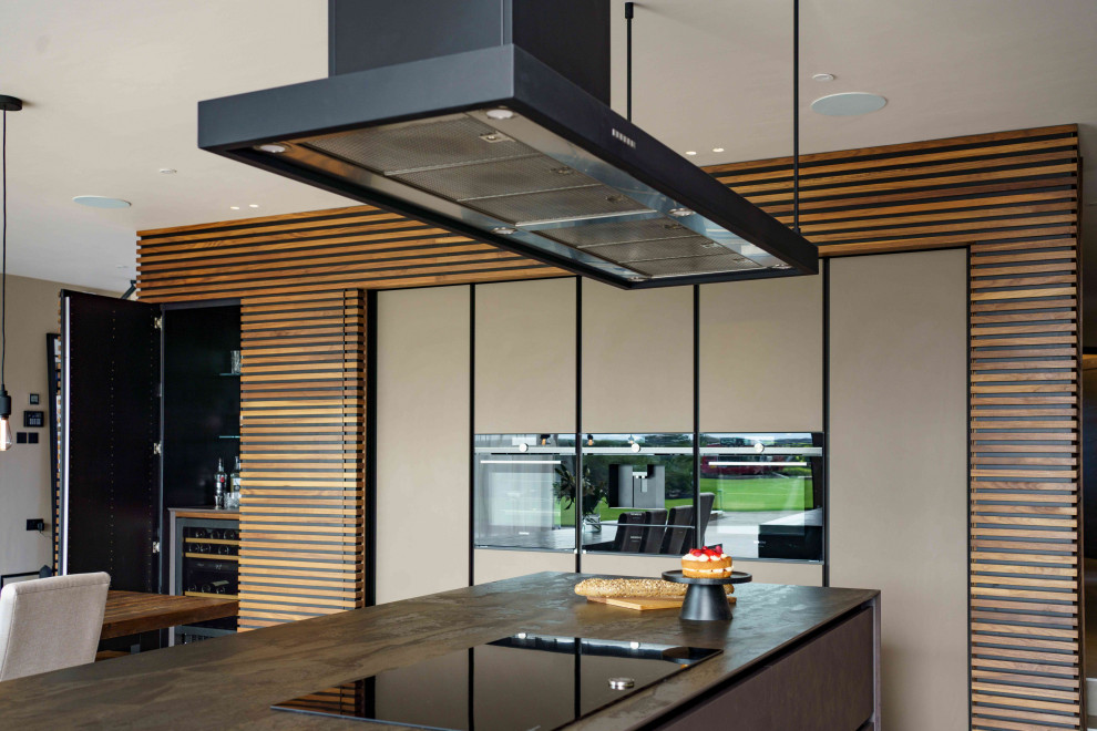 Inspiration for a large contemporary l-shaped kitchen/diner in Cardiff with flat-panel cabinets, mirror splashback, black appliances and an island.
