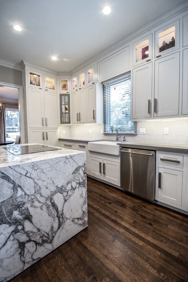 Enclosed kitchen - large transitional l-shaped dark wood floor enclosed kitchen idea with a farmhouse sink, shaker cabinets, white cabinets, solid surface countertops, white backsplash, subway tile backsplash, stainless steel appliances and an island