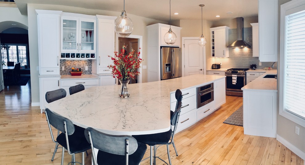 Mid-sized transitional light wood floor kitchen photo with an undermount sink, shaker cabinets, white cabinets, quartz countertops, blue backsplash, glass tile backsplash, stainless steel appliances and an island