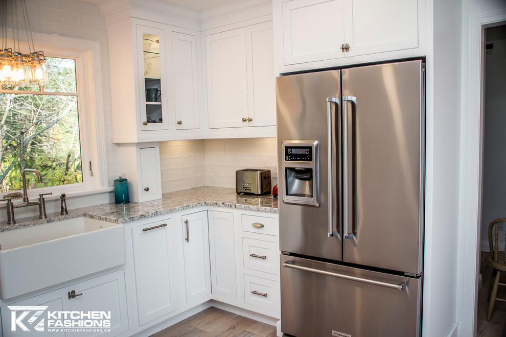 Example of a large transitional u-shaped light wood floor eat-in kitchen design with a farmhouse sink, shaker cabinets, white cabinets, granite countertops, white backsplash, subway tile backsplash, stainless steel appliances and no island