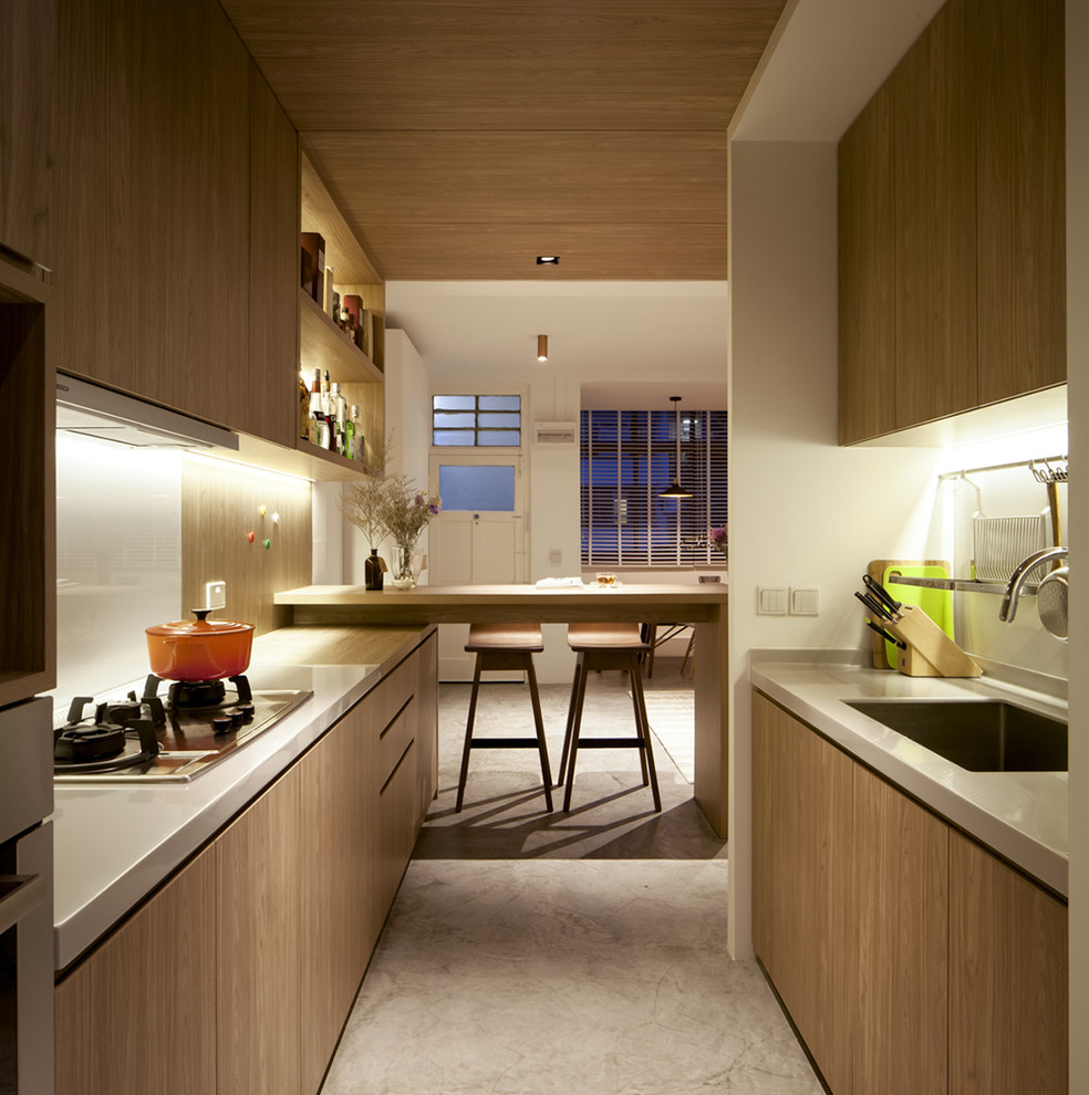 Photo of a contemporary galley kitchen in Singapore with a single-bowl sink, flat-panel cabinets, light wood cabinets, white splashback, glass sheet splashback and a peninsula.