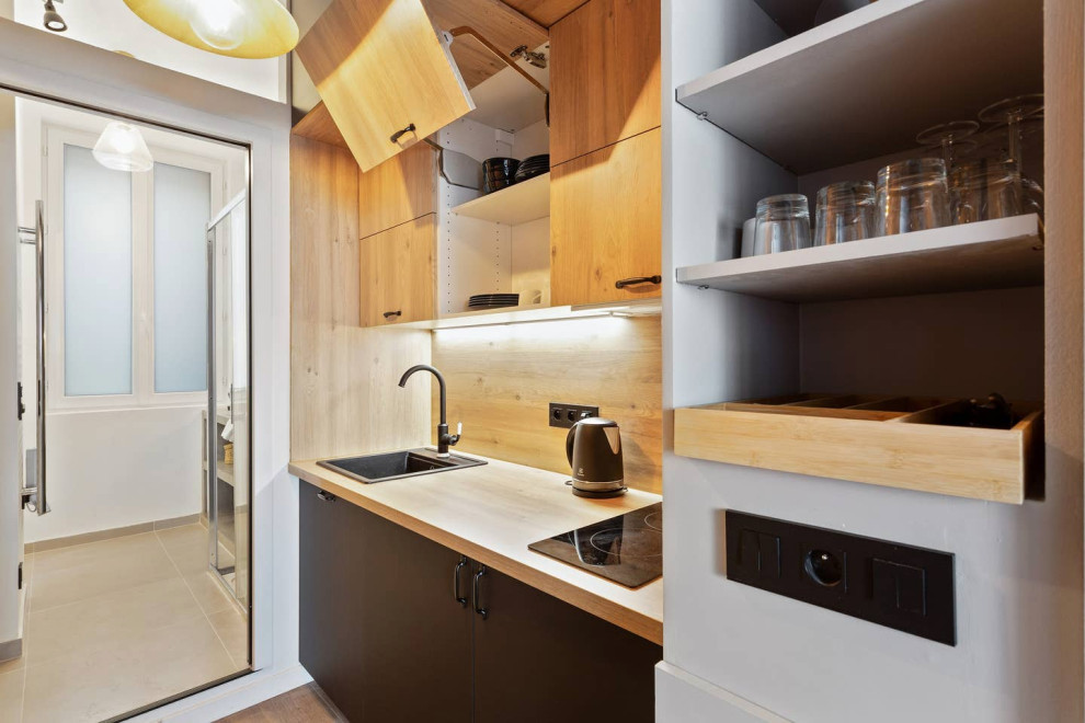 Inspiration pour une petite cuisine ouverte linéaire urbaine avec un évier encastré, des portes de placard noires, un plan de travail en bois, une crédence en bois et un électroménager noir.