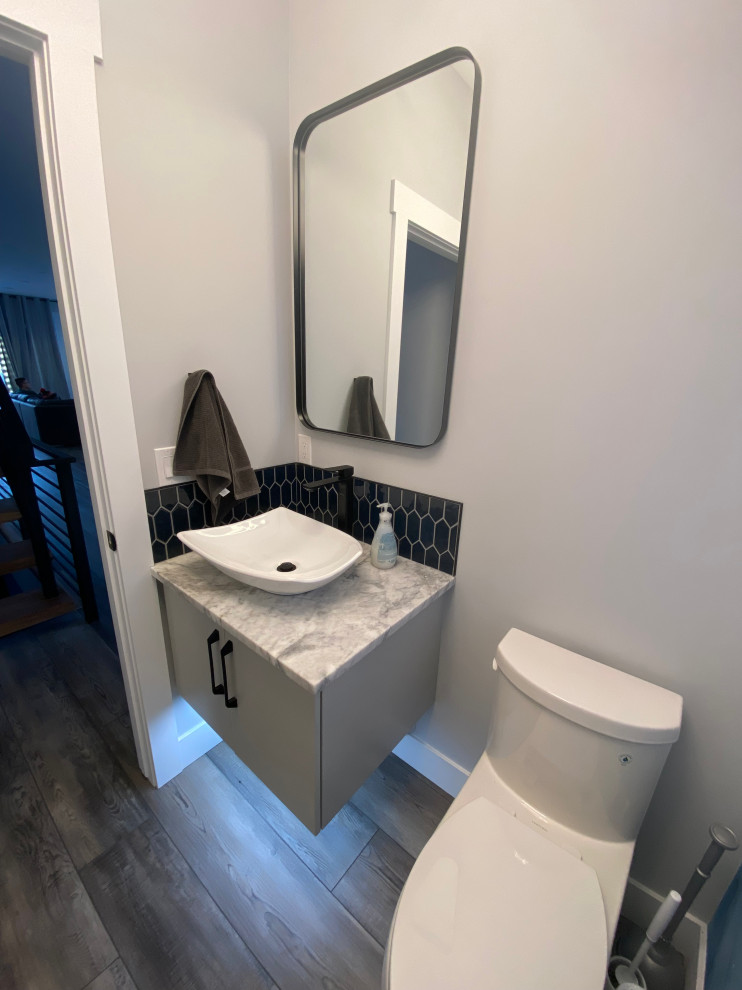 Photo of a small contemporary powder room in Calgary with flat-panel cabinets, grey cabinets, a one-piece toilet, blue tile, ceramic tile, blue walls, vinyl floors, an undermount sink, granite benchtops, brown floor, white benchtops, a built-in vanity and wallpaper.
