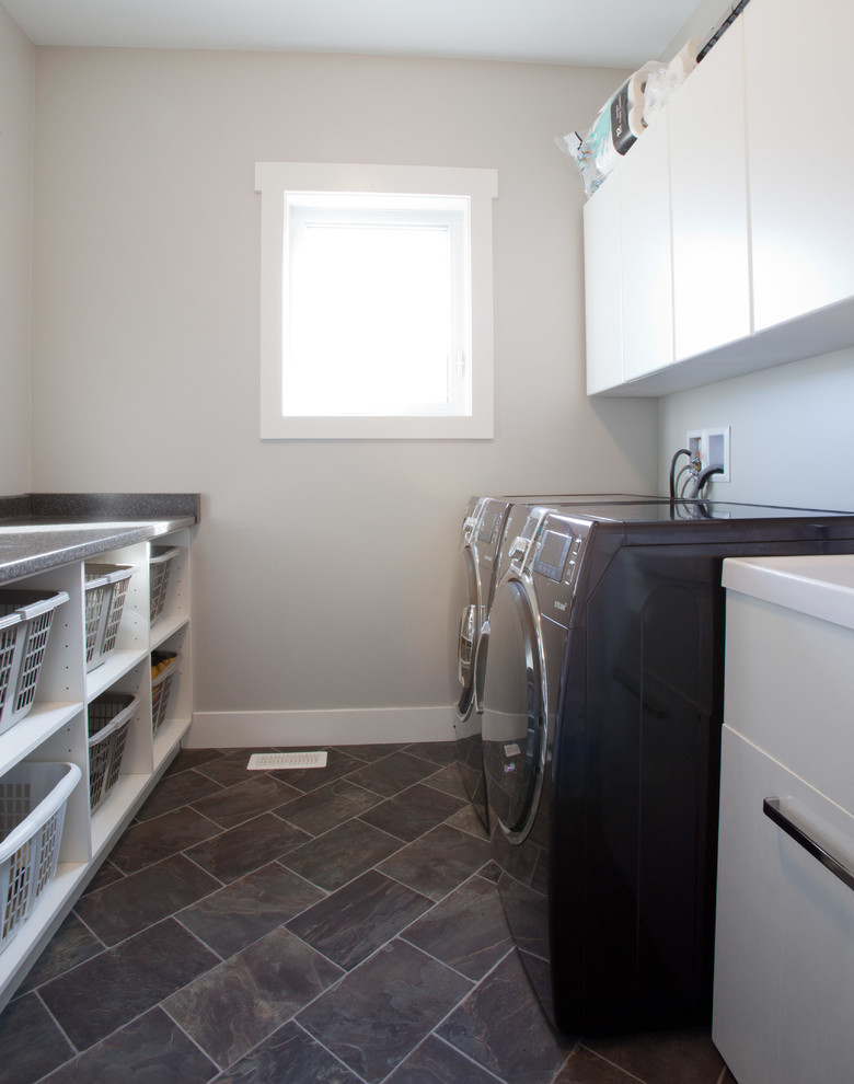 Inspiration for a mid-sized traditional galley dedicated laundry room in Vancouver with flat-panel cabinets, white cabinets, laminate benchtops, grey walls, a side-by-side washer and dryer and slate floors.
