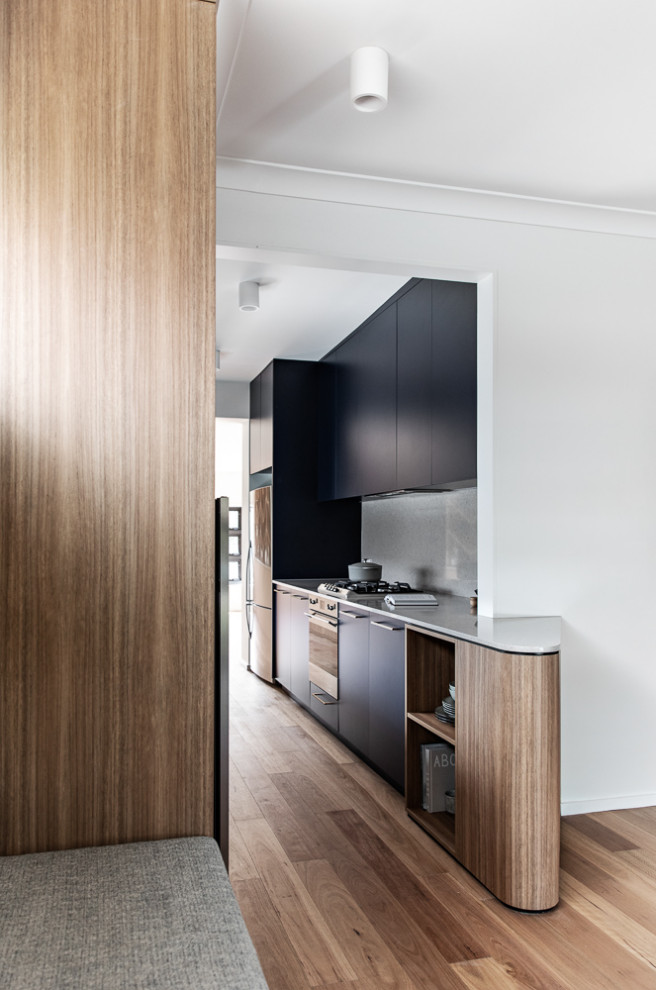 Mid-sized contemporary galley separate kitchen in Sydney with a double-bowl sink, blue cabinets, quartz benchtops, grey splashback, engineered quartz splashback, stainless steel appliances, medium hardwood floors, no island, brown floor and grey benchtop.