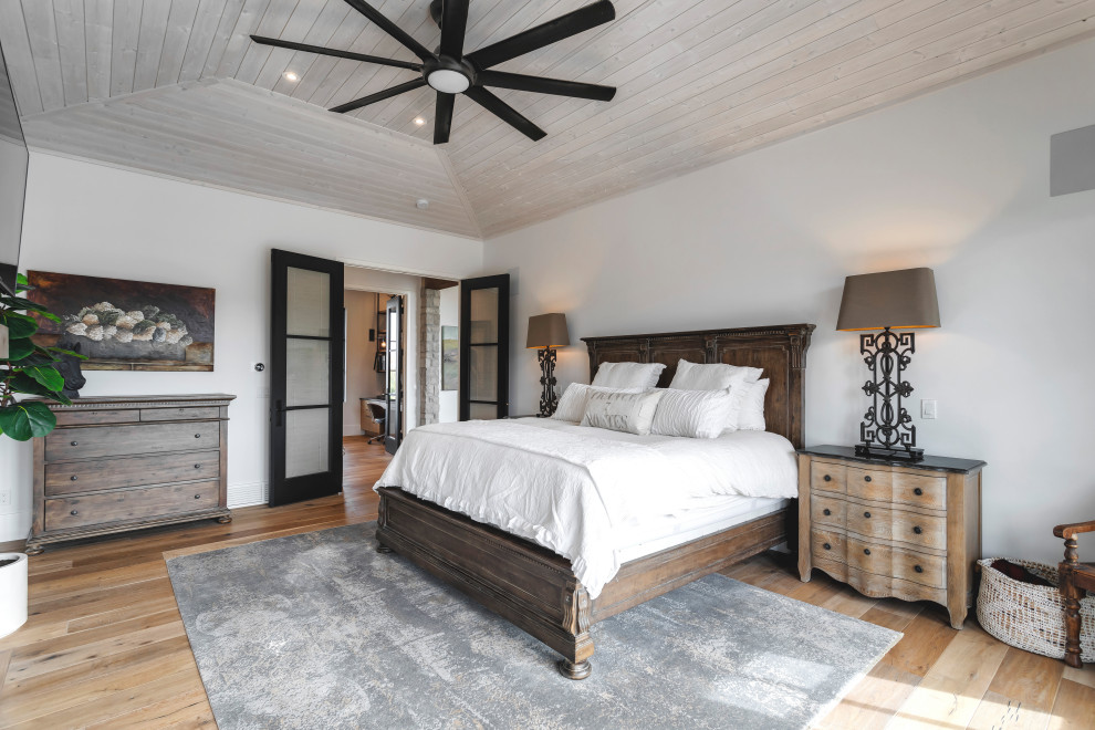Modelo de dormitorio principal tradicional renovado grande con paredes blancas, suelo de madera oscura, chimenea de doble cara, marco de chimenea de yeso y bandeja