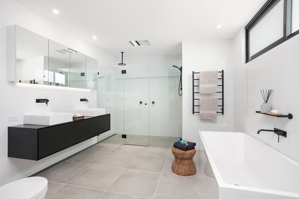 Photo of a contemporary master bathroom in Sydney with black cabinets, a freestanding tub, a one-piece toilet, white tile, ceramic tile, white walls, ceramic floors, a vessel sink, solid surface benchtops, grey floor, a hinged shower door, black benchtops, flat-panel cabinets and an alcove shower.