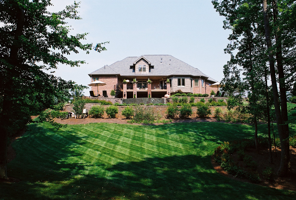 Photo of a large partial sun backyard stone retaining wall landscape.