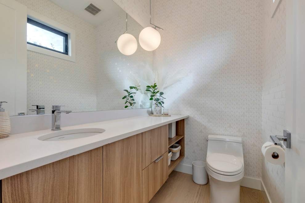 Foto på ett funkis vit toalett, med släta luckor, skåp i mellenmörkt trä, en toalettstol med hel cisternkåpa, vita väggar, vinylgolv, ett undermonterad handfat, bänkskiva i kvarts och brunt golv