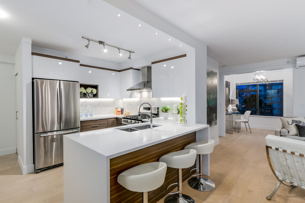 Mid-sized contemporary u-shaped eat-in kitchen in Vancouver with an undermount sink, flat-panel cabinets, white cabinets, quartz benchtops, white splashback, porcelain splashback, stainless steel appliances, light hardwood floors and a peninsula.
