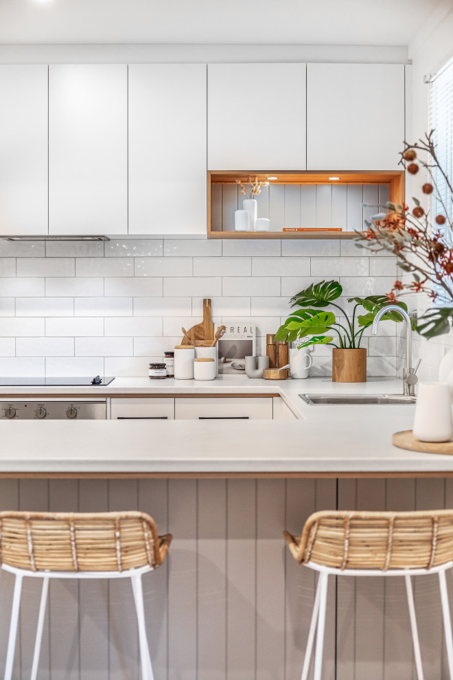 Photo of a mid-sized contemporary u-shaped eat-in kitchen in Adelaide with a single-bowl sink, white cabinets, laminate benchtops, white splashback, subway tile splashback, stainless steel appliances, medium hardwood floors, a peninsula, brown floor and white benchtop.