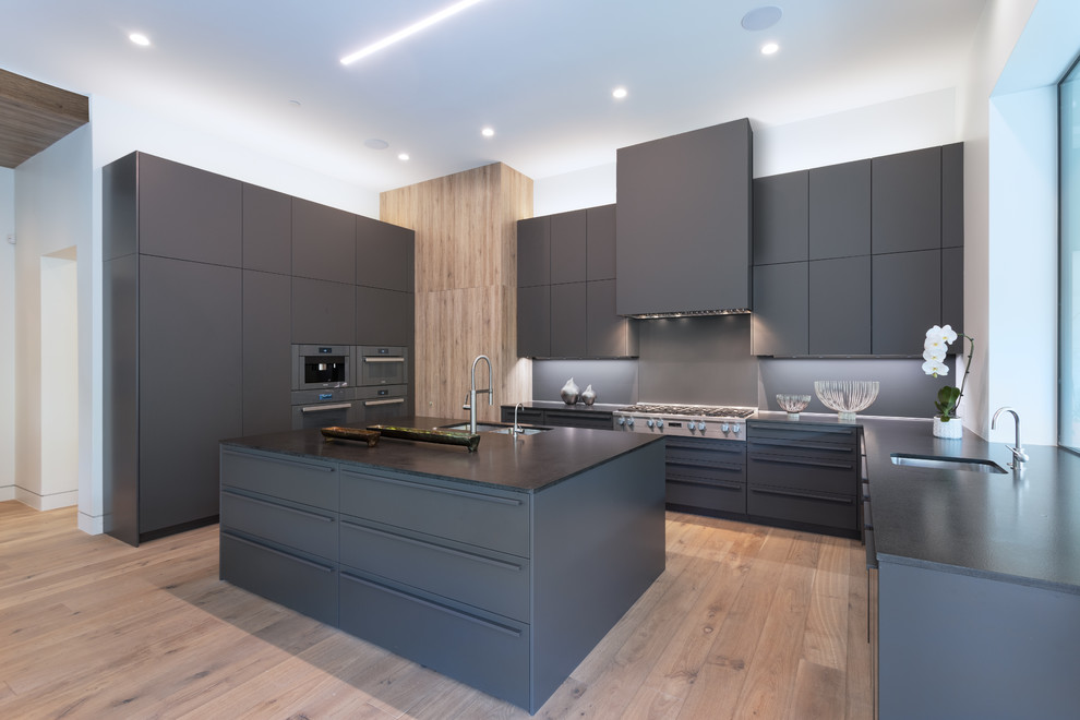 Photo of a contemporary u-shaped kitchen in Austin with an undermount sink, flat-panel cabinets, grey cabinets, stainless steel appliances, medium hardwood floors, with island, brown floor and black benchtop.