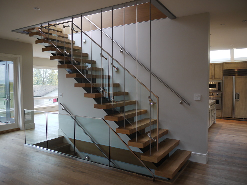 This is an example of a mid-sized modern wood floating staircase in Vancouver with open risers and glass railing.