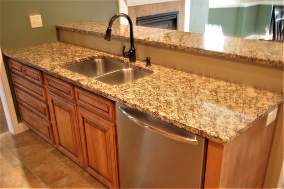 Inspiration for a mid-sized timeless l-shaped porcelain tile and brown floor enclosed kitchen remodel with an undermount sink, raised-panel cabinets, light wood cabinets, granite countertops, stainless steel appliances and a peninsula