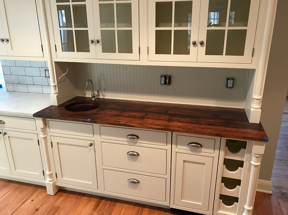 Inspiration for an expansive country l-shaped wet bar in Philadelphia with beige cabinets, wood benchtops, beige splashback, timber splashback, an undermount sink, glass-front cabinets and medium hardwood floors.