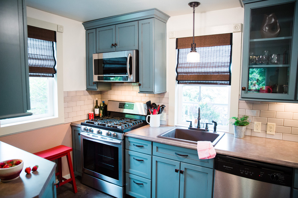 This is an example of a mid-sized traditional galley separate kitchen in Seattle with a drop-in sink, flat-panel cabinets, blue cabinets, laminate benchtops, grey splashback, porcelain splashback, stainless steel appliances, vinyl floors and no island.