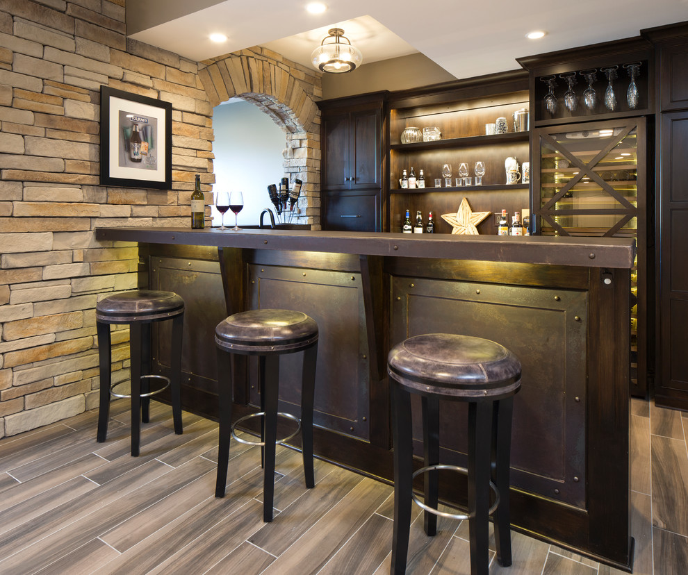 This is an example of a mid-sized industrial single-wall seated home bar in Chicago with dark wood cabinets, stainless steel benchtops, porcelain floors, brown floor and shaker cabinets.