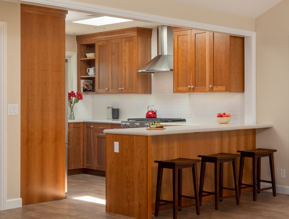 This is an example of a mid-sized transitional l-shaped separate kitchen in San Francisco with a drop-in sink, shaker cabinets, medium wood cabinets, quartz benchtops, white splashback, ceramic splashback, stainless steel appliances, medium hardwood floors, a peninsula, brown floor and white benchtop.