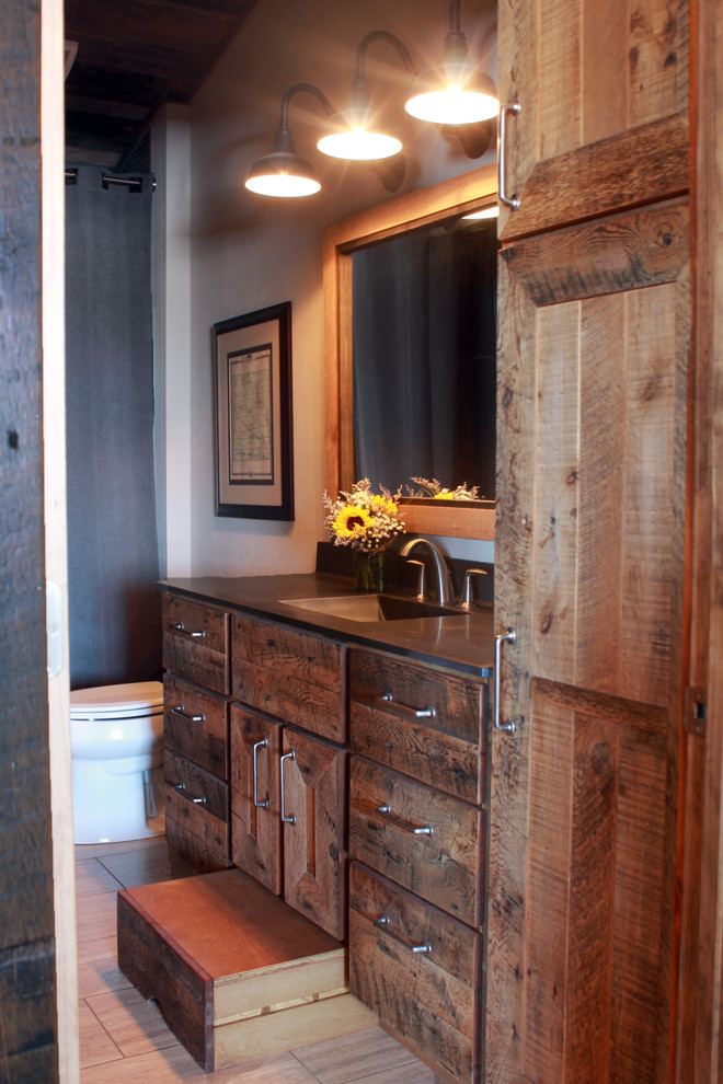 Photo of a mid-sized country master bathroom in Other with an integrated sink, recessed-panel cabinets, distressed cabinets, concrete benchtops, an alcove tub, a shower/bathtub combo, a two-piece toilet, grey walls and limestone floors.