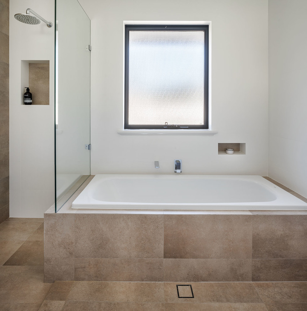 Photo of a mid-sized contemporary master bathroom in Perth with grey cabinets, a drop-in tub, white tile, white walls, ceramic floors, an undermount sink, solid surface benchtops, beige floor and a hinged shower door.