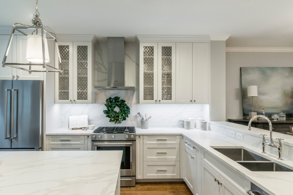 Inspiration for a small transitional l-shaped medium tone wood floor and brown floor kitchen remodel in Houston with a double-bowl sink, shaker cabinets, white cabinets, quartz countertops, white backsplash, stone slab backsplash, stainless steel appliances, an island and white countertops
