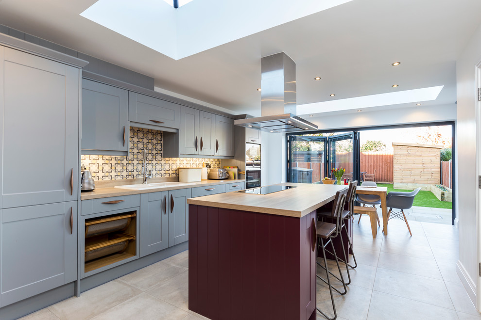 Inspiration for a large transitional single-wall eat-in kitchen in London with a double-bowl sink, shaker cabinets, blue cabinets, wood benchtops, multi-coloured splashback, with island, ceramic splashback, stainless steel appliances and ceramic floors.