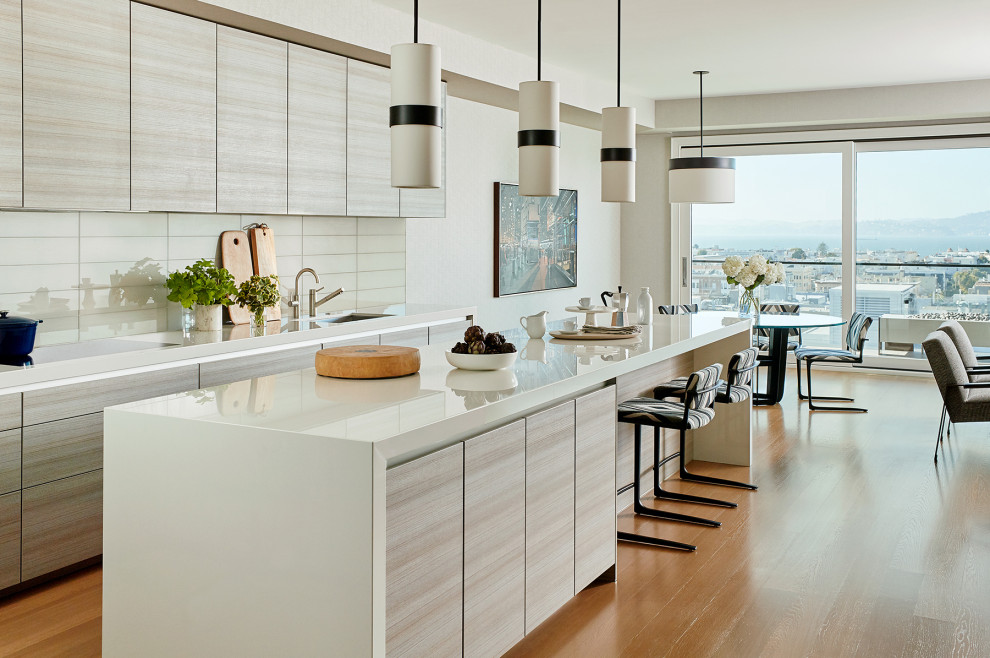 Photo of a mid-sized contemporary galley eat-in kitchen in San Francisco with an undermount sink, flat-panel cabinets, light wood cabinets, quartz benchtops, stainless steel appliances, medium hardwood floors, with island and white benchtop.