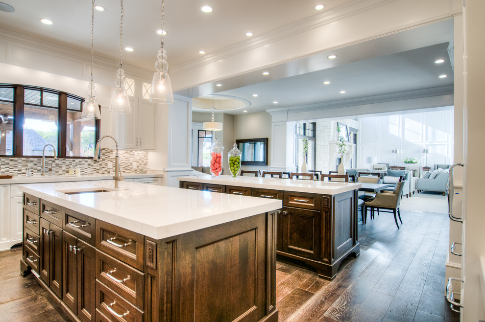 Photo of an expansive traditional l-shaped open plan kitchen in Salt Lake City with an undermount sink, recessed-panel cabinets, white cabinets, quartzite benchtops, multi-coloured splashback, ceramic splashback, white appliances, dark hardwood floors and multiple islands.