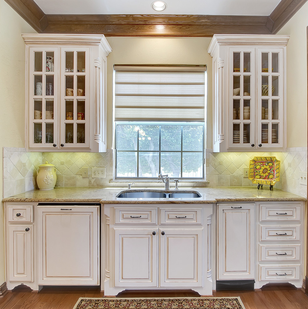 Design ideas for a traditional kitchen in Dallas with a double-bowl sink, glass-front cabinets, white cabinets and beige splashback.