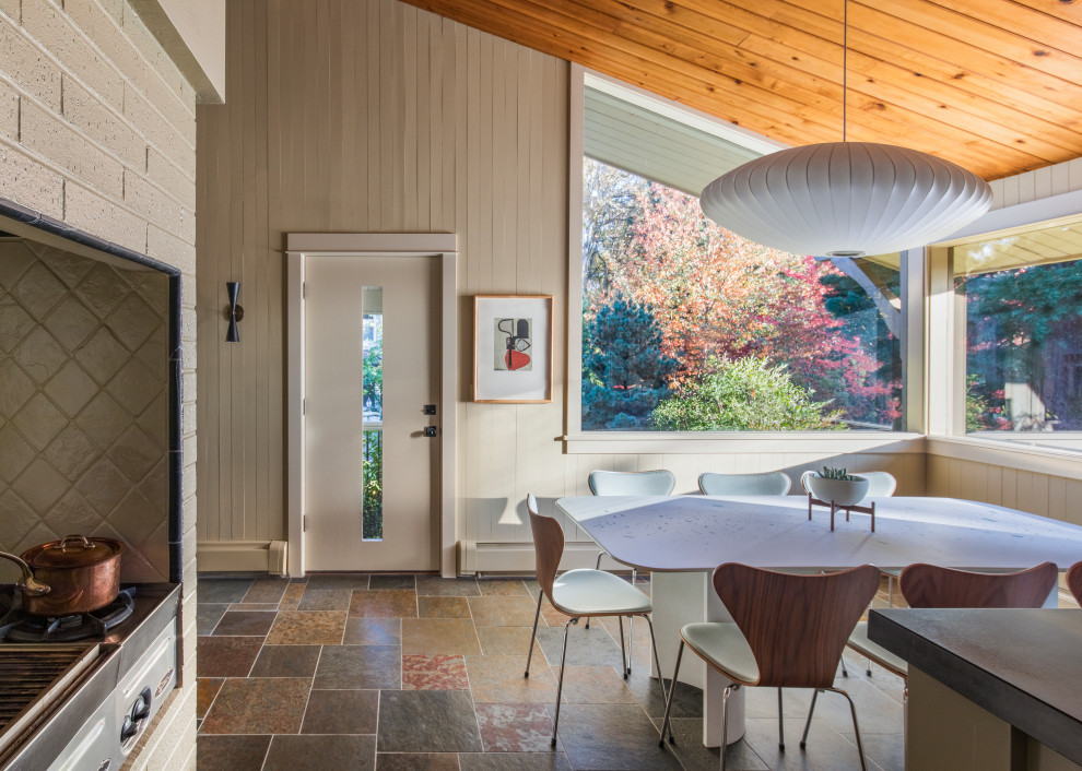 This is an example of a large midcentury l-shaped eat-in kitchen in Portland with a double-bowl sink, flat-panel cabinets, beige cabinets, granite benchtops, multi-coloured splashback, slate splashback, stainless steel appliances, slate floors, with island, brown floor and black benchtop.