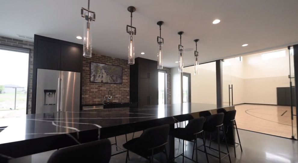 Photo of an expansive industrial home bar in Other with an undermount sink, flat-panel cabinets, black cabinets, quartz benchtops, brick splashback, concrete floors and black benchtop.