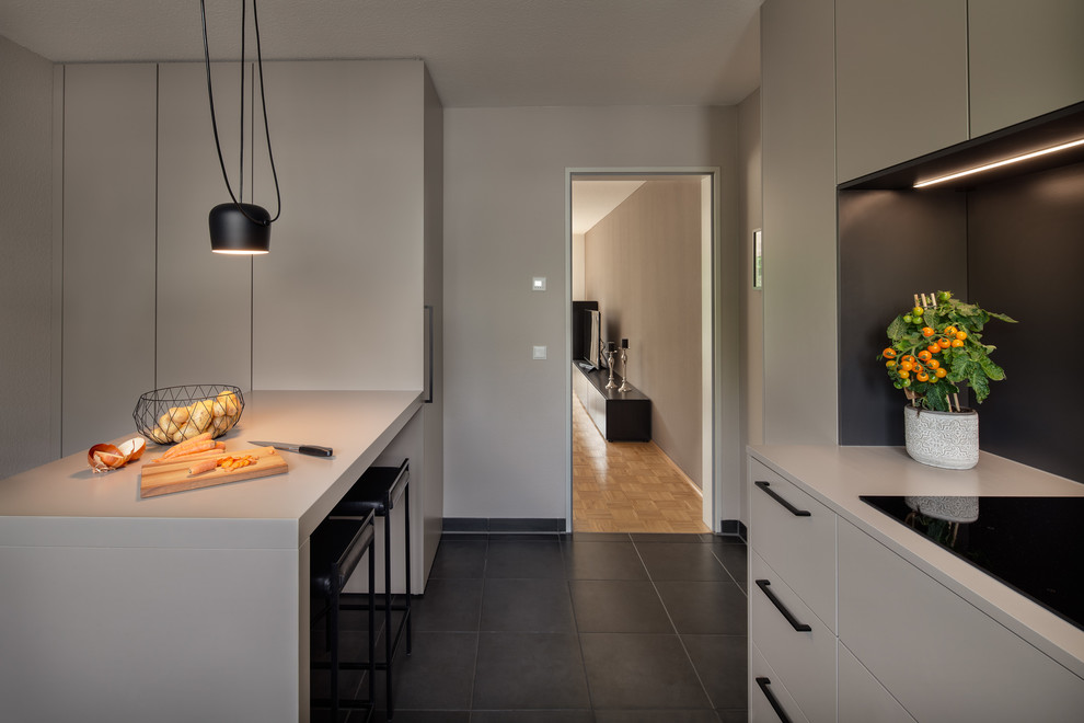 Photo of a large modern l-shaped open plan kitchen in Cologne with an integrated sink, flat-panel cabinets, grey cabinets, solid surface benchtops, black splashback, timber splashback, stainless steel appliances, cement tiles, with island, black floor and grey benchtop.
