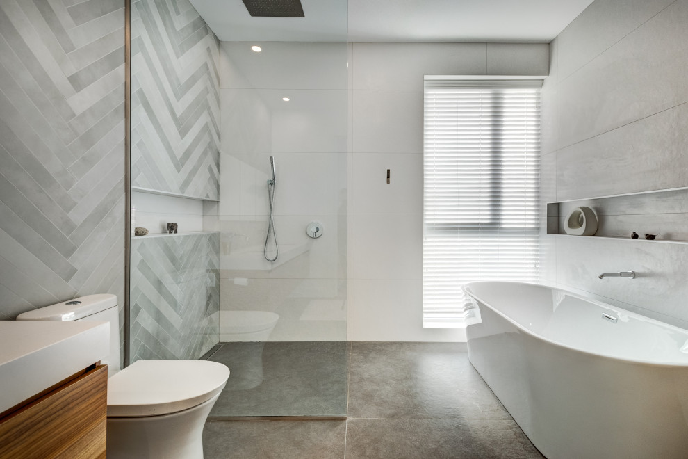 Inspiration for a contemporary bathroom in Austin with flat-panel cabinets, medium wood cabinets, a freestanding tub, a curbless shower, gray tile, grey floor, an open shower and white benchtops.