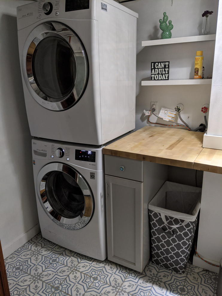 Small transitional dedicated laundry room in Denver with wood benchtops, ceramic floors and a stacked washer and dryer.