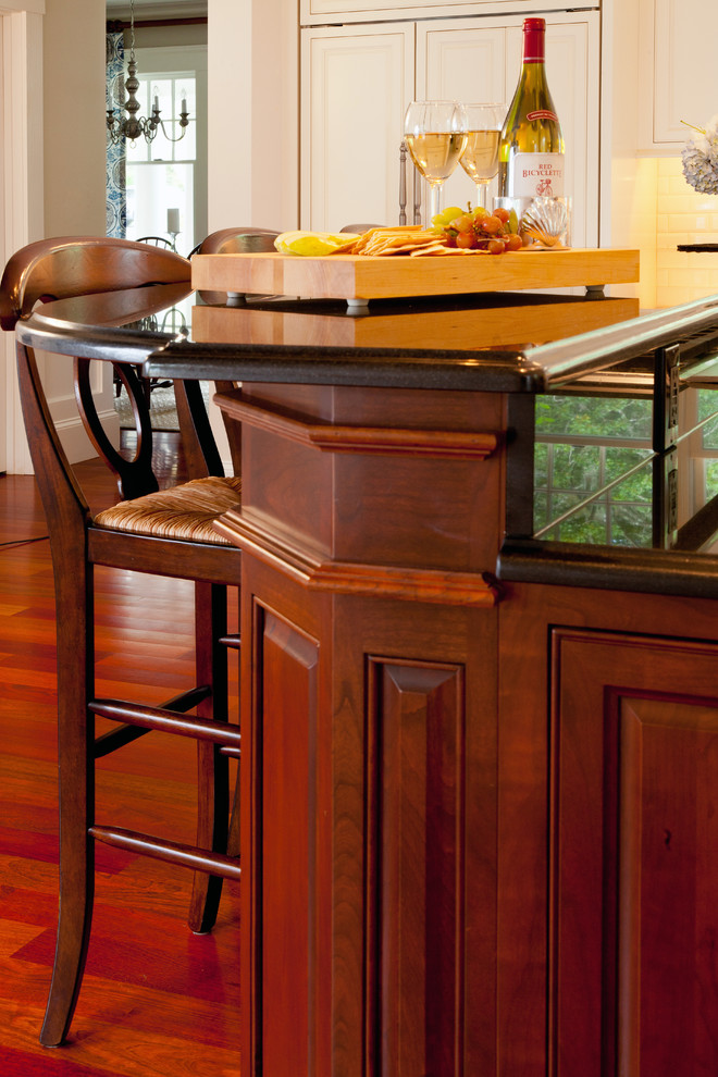 Eat-in kitchen - transitional l-shaped medium tone wood floor eat-in kitchen idea in Boston with an undermount sink, raised-panel cabinets, white cabinets, granite countertops, white backsplash, ceramic backsplash, stainless steel appliances and an island