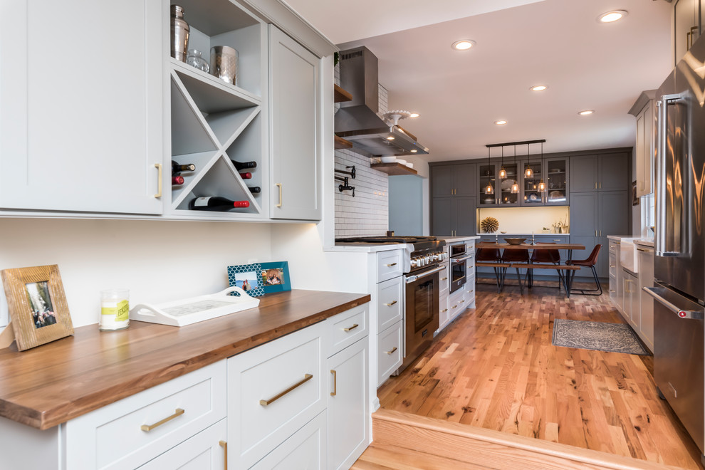 Mid-sized transitional galley medium tone wood floor eat-in kitchen photo in Denver with a farmhouse sink, shaker cabinets, gray cabinets, quartz countertops, white backsplash, porcelain backsplash, stainless steel appliances, a peninsula and white countertops