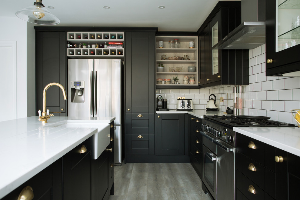 Design ideas for a transitional kitchen in London with a farmhouse sink, shaker cabinets, black cabinets, white splashback, subway tile splashback, stainless steel appliances, with island, grey floor and white benchtop.