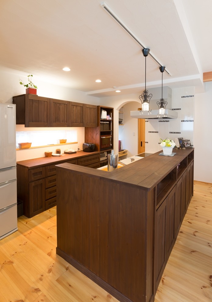 Design ideas for an asian galley open plan kitchen in Other with an integrated sink, recessed-panel cabinets, dark wood cabinets, wood benchtops, white splashback, medium hardwood floors, with island and brown floor.